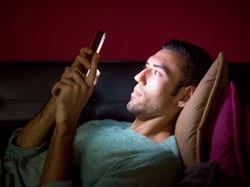 Man looking at a smart phone in bed